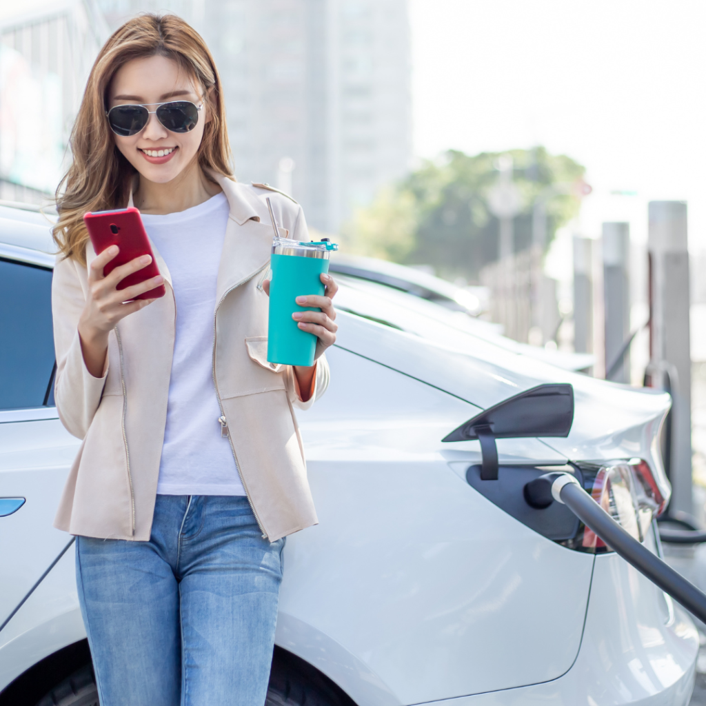 Woman Using Smartphone at the Electric Vehicle Charging Station