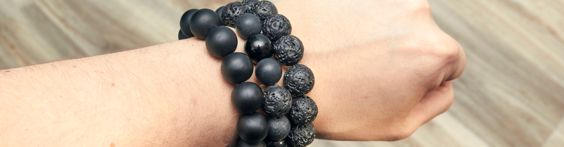 three black shungit lava bracelets on the background of a wooden floor are dressed on a hand⁠