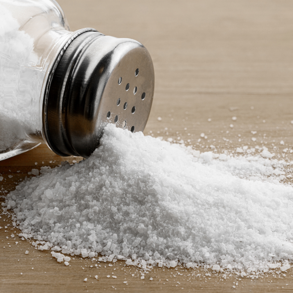 Salt glass jar and pile of spilled salt on a wooden table