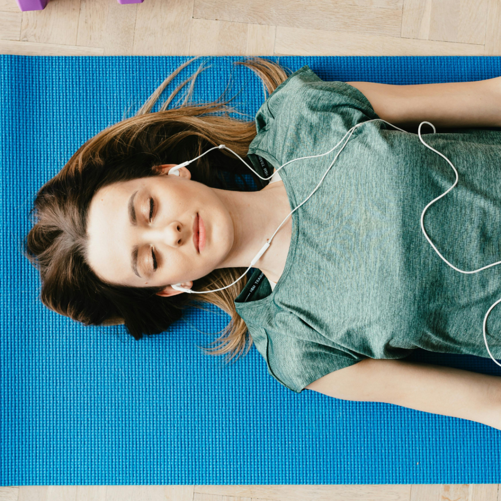 Peaceful woman in earphones resting in Shavasana pose at home