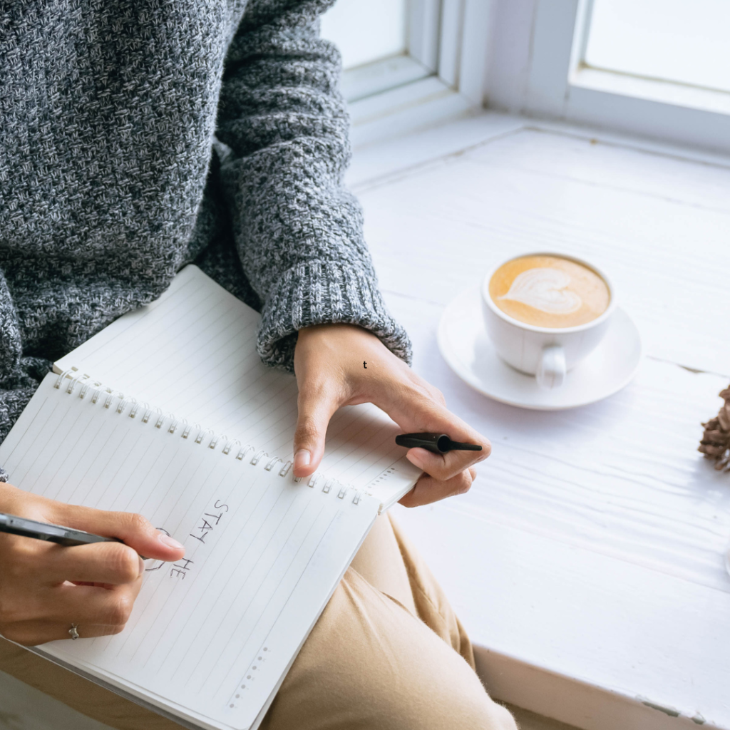 Person Writing on a Notebook by the Windowsill