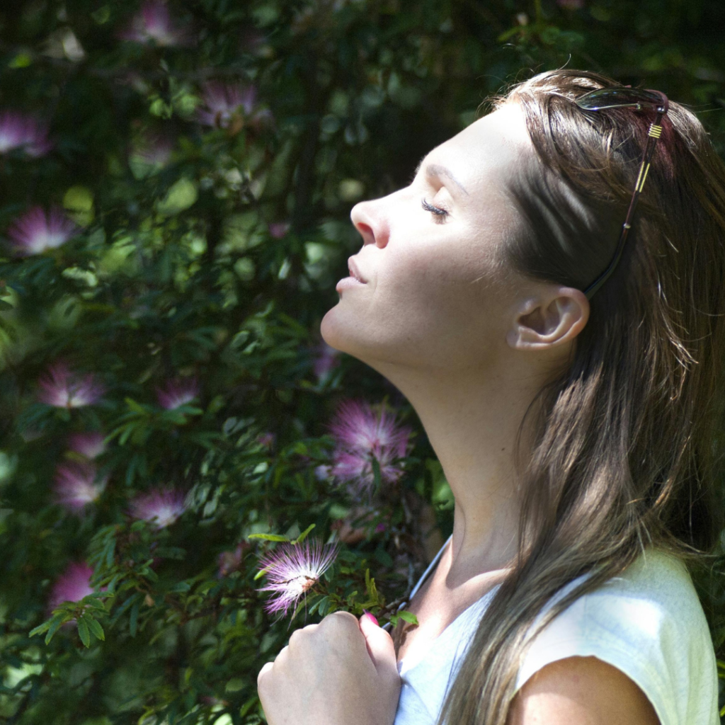 Woman Closing Her Eyes Against Sun Light Standing Near Purple Petaled Flower Plant