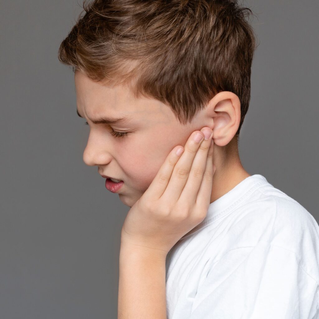 Teenage boy with pained expression holding his sore ears